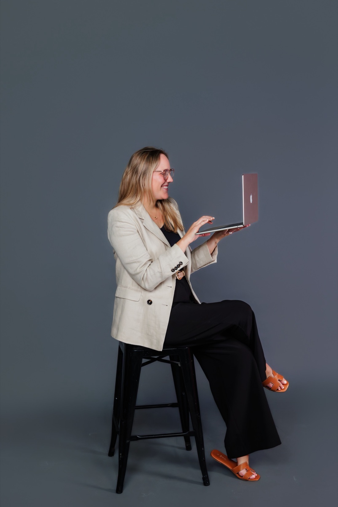 Lucia sitting on a stool with her laptop, smiling